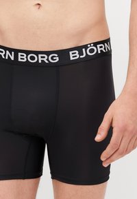 Schwarze Boxer Shorts mit einer weichen, glatten Textur und einem breiten schwarzen Bund, der den weißen Schriftzug "BJÖRN BORG" trägt. Körpernaher Schnitt.