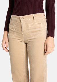 Pantalon en velours côtelé beige à coupe droite, avec poches avant et taille fermée par un bouton. Associé à un haut à manches longues côtelé de couleur bordeaux.