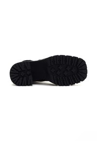 Suela de zapato de goma negra con surcos profundos para tracción, que cuenta con una superficie texturizada y bordes definidos, diseñada para durabilidad y agarre.
