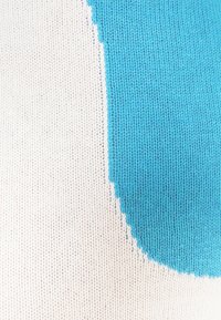 Gros plan d’un tissu tricoté avec une grande forme incurvée bleue sur un fond blanc montrant la texture détaillée des mailles.