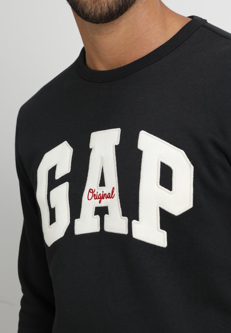 Schwarzer Sweatshirt mit Rundhalsausschnitt, featuring große weiße Buchstaben "GAP" und das Wort "Original" in roten, gestickten Details. Weicher Baumwollstoff.