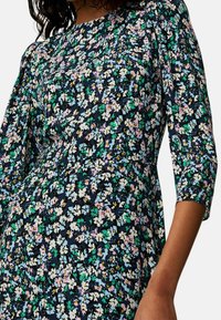Abito floreale in blu navy, con una miscela di fiori colorati in rosa, verde e bianco. Maniche lunghe e tessuto morbido e testurizzato.