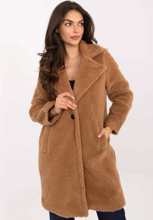 Beżowy, puszysty płaszcz o długim kroju z wyciętym kołnierzem, pojedynczym zapięciem na guzik i bocznymi kieszeniami, na jasnym tle.