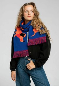 Szydełkowany szalik w kolorze niebieskim z pomarańczowymi sylwetkami psów. Posiada czerwone frędzle na brzegach. Miękka faktura, duży rozmiar i zabawny design.