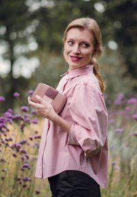 Light pink shirt with puffed sleeves, paired with a neutral wallet. Set in a field with purple flowers and blurred green background.