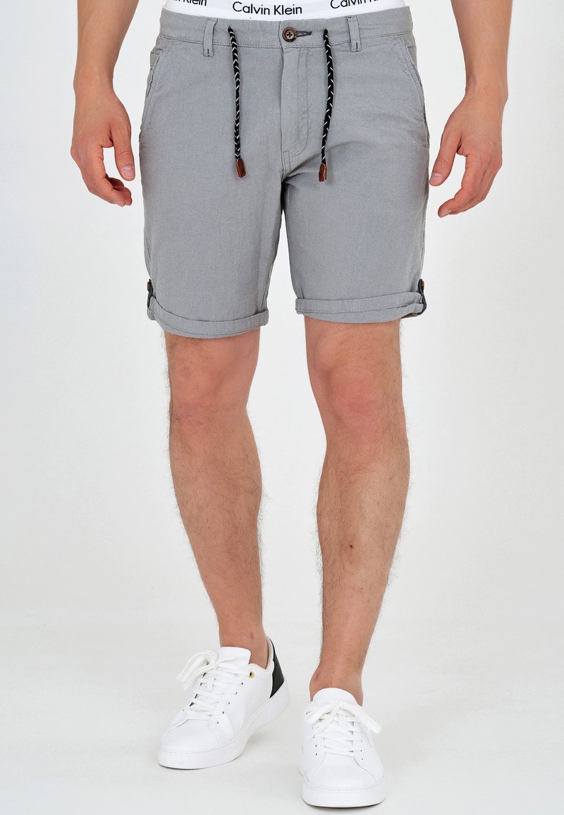 Graue Baumwollshorts mit umgeschlagenen Säumen, ausgestattet mit einem Kordelzugverschluss mit Lederakzenten. Getragen mit weißen Turnschuhen und einem Calvin Klein Bund.