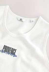 Canottiera bianca in cotone con finitura testurizzata, con la scritta "PROVENCE" ricamata in nero e blu sul petto. Etichetta taglia media visibile.