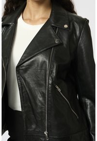Svart lädermotorcykeljacka med slagkrage, silverdetaljer, två fickor med blixtlås och en figurnära silhuett. Texturerad yta.