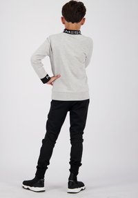 Chemise grise à manches longues avec un col noir portant un texte blanc, associée à un pantalon de jogging noir et des chaussures de sport noires avec des semelles blanches.