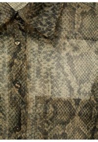 Chemise légère avec un motif en cuir de serpent dans des nuances de gris et de beige. Dotée d'un col et d'une fermeture par bouton, avec une poche poitrine.