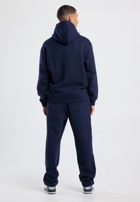 Sudadera y pantalones de chándal azul marino de tejido suave con un corte relajado. La sudadera cuenta con un gran bolsillo canguro y cordones ajustables.