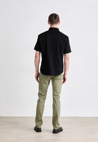 Crna majica kratkih rukava s ovratnikom, uparena s maslinasto zelenim hlačama. Outfit ima opušteni kroj i minimalne dizajnerske detalje.