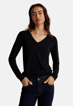 Maglione nero a collo a V in tessuto morbido, maniche lunghe, design aderente, abbinato a jeans scuri con cuciture arancioni e tasche frontali.