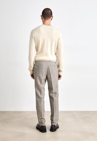 Krémový měkký svetr s kulatým výstřihem, zkombinovaný se světle šedými skládacími kalhotami s dvěma zakřivenými zadními kapsami. Look doplňují tmavé boty.