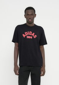 Μαύρο βαμβακερό μπλουζάκι με κόκκινο κείμενο "ADIDAS 1994" σε κυρτό σχέδιο. Κανονική εφαρμογή με κοντά μανίκια και κλασικό λαιμόκοψη.