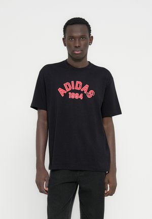 Svart bomulls-T-skjorte med rød "ADIDAS 1994"-tekst i en buet design. Vanlig passform med korte ermer og klassisk rund hals.