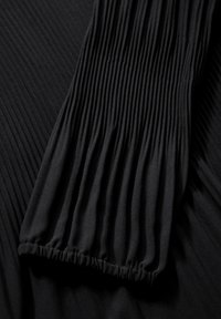 Tissu noir avec une texture plissée, doté d'un poignet froncé. Un matériau lisse et fluide tombe avec un subtil éclat sur les détails de surface.