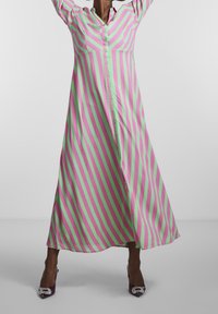 Robe longue rayée présentant de vives lignes roses et vertes, avec un design à boutons sur le devant et un tissu doux. Assortie avec des talons accentués en violet.