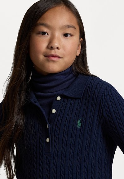 Σκούρο μπλε πουλόβερ με πλέξη καλωδίων, με αναδιπλούμενο γιακά, που διαθέτει τρία λευκά κουμπιά και ένα μικρό πράσινο λογότυπο στο στήθος. Μαλακή υφή.