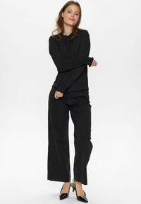 Top nero a maniche lunghe con scollatura arricciata, abbinato a pantaloni neri a righe larghe e tacchi a punta neri, creando una silhouette elegante.