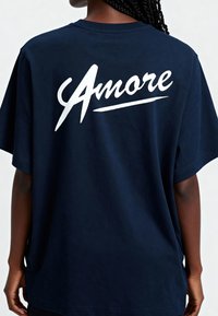 Tums zila kokvilnas T-krekls ar brīvu piegriezumu, uz muguras ar baltu "Amore" tekstu kursīvā. Mīksta tekstūra, īsas piedurknes, apaļa kakla izgriezums.