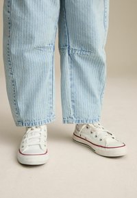 Baskets en toile blanches avec des accents rouges, portées avec un jean à rayures bleu clair, à coupe ample et longueur cropped.
