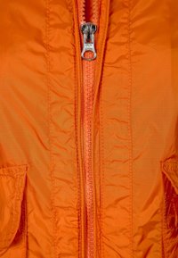 Orange pufferjacka med en glansig dragkedja, sömnadsdetaljer, två sidofickor och ett lätt, texturerat tyg.