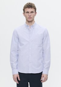 Button-up shirt in blue and white stripes, long sleeves, collar, and a small logo on the chest. Cotton fabric with smooth texture.