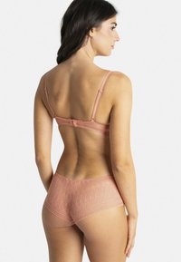 Ensemble soutien-gorge et slip en dentelle rose pâle, avec des bords délicatement festonnés, des bretelles ajustables et une fermeture au dos. Tissu texturé.
