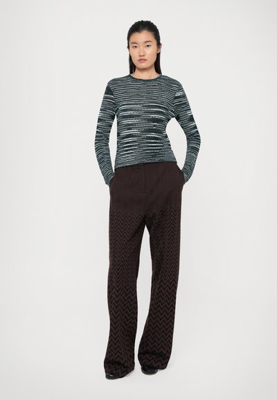 Top lung cu maneci lungi, în dungi negre și teal, cu siluetă ajustată, asortat cu pantaloni largi cu zigzaguri maronii.