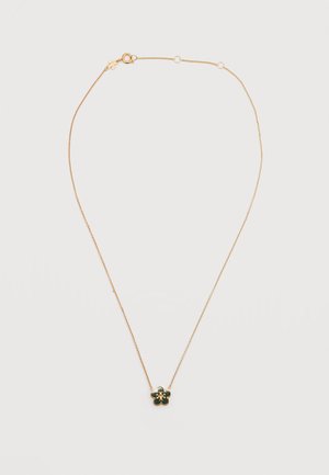 Delikatny naszyjnik z złotym łańcuszkiem z małym ciemnozielonym wisiorkiem w kształcie kwiatu z złotym emblematem w środku na białym tle.