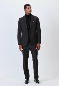 Ciemny garnitur ze slim fit, z czarnym golfem. Marynarka ma satynowe wyłogi i poszetkę. Czarne buty dopełniają outfit.