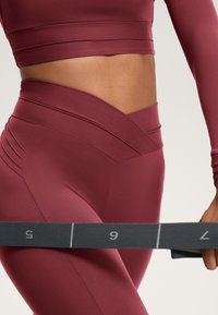 Bordeaux actieve set bestaande uit een aansluitende langharige crop-top en hoge taille leggings met getextureerde details aan de zijkant.