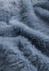 Szürke műszőrme textil, plüss, bolyhos textúrával és változó kék árnyalatokkal, puha, hosszú szálakkal, amelyek hullámokban rendeződnek.