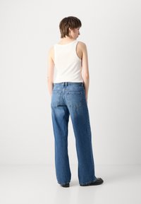 Jeans en denim bleu clair à jambe large avec une coupe droite, cinq poches et une taille haute ; associés à un débardeur blanc ajusté.