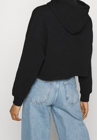 Sudadera corta negra con capucha ajustable, combinada con jeans de pierna ancha de color azul claro, que presentan una textura de mezclilla clásica y diseño de bolsillo trasero.