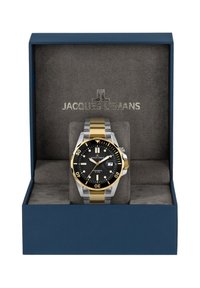 Reloj de acero inoxidable y oro en una caja de presentación azul. La esfera negra cuenta con marcadores luminosos, indicador de fecha y bisel giratorio.