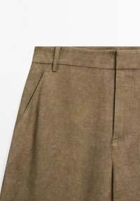 Pantaloni khaki con una texture liscia, taglio dritto, tasche frontali e passanti per cintura. Il tessuto ha una finitura opaca sottile.