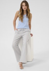 Svijetloplava rebrasta majica bez rukava u kombinaciji s bijelim laganim širokim hlačama sa prugama, koje imaju elastiku u struku i bočne džepove.