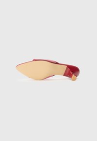 Red patent leather high-heeled shoe with a pointed toe, contrasting beige sole, and a textured finish along the upper section.