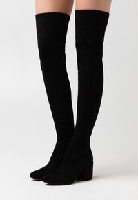 Bottes noires montant jusqu'en haut des cuisses, en daim souple, avec un talon bloc poli, un bout pointu et une fermeture éclair latérale pour un enfilage facile.