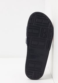 Schwarze Gummisohle mit strukturiertem Muster und Logo. Die Seite verfügt über ein atmungsaktives Mesh-Obermaterial in Marineblau, Rot und weißen Streifen.