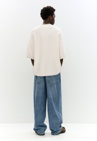Maglietta a maglia texturizzata oversize di colore bianco sporco con vestibilità rilassata, abbinata a jeans di denim blu larghi, con lavaggio chiaro e tasche posteriori.