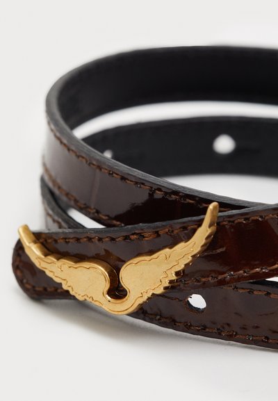 Bruine gepolijste leren riem met gouden vleugelvormige hardware, voorzien van een gladde textuur en meerdere verstelgaten voor maataanpassing.