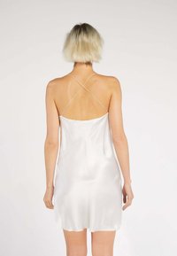 White satin slip dress with thin, crisscross straps at the back, featuring a smooth texture and a flowing silhouette.