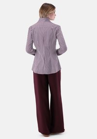 Il blazer a righe presenta righe verticali bordeaux e bianche, taglio su misura, colletto alto, abbinato a pantaloni bordeaux a gamba larga. Tessuto dalla trama liscia.