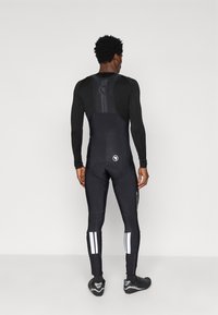 Čierny celový cyklistický overal s priliehavým strihom, ktorý má pretekársku zadnú časť, reflexné pruhy a textúrovanú tkaninu pre lepší úchop.