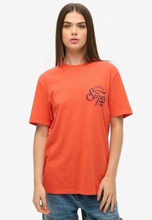 T-shirt en coton orange à manches courtes et col rond. Présente un logo imprimé bleu marine sur le côté gauche. Coupe décontractée.