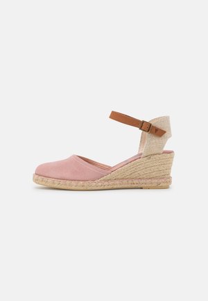 Sandale compensée en daim rose avec une semelle intermédiaire en jute tressé, une sangle de cheville réglable en cuir tan et une sangle de talon en tissu beige texturé.