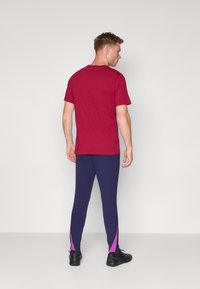 Rød kortærmet t-shirt parret med marineblå ribbede leggings med lilla detaljer på siden. Sorte sportssko fuldender outfittet.